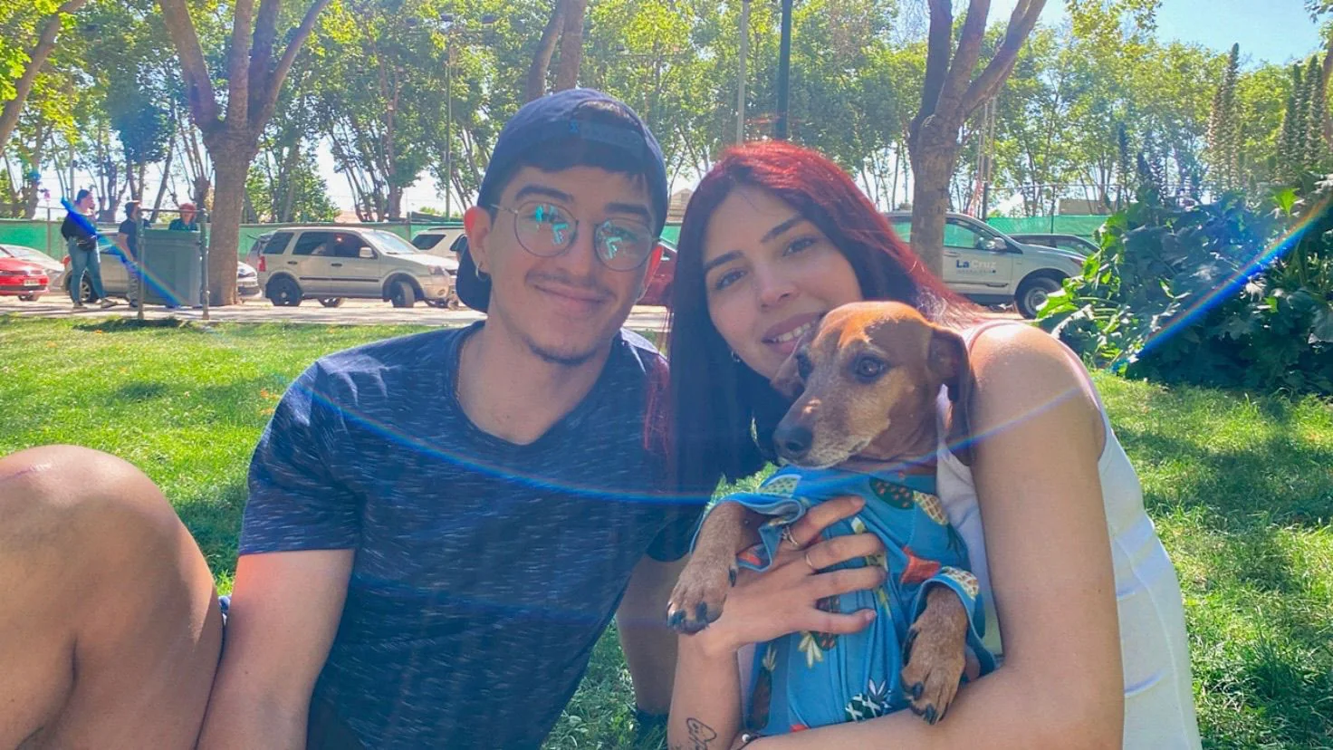 Maximiliano y Javiera sentados en el parque junto a su perro